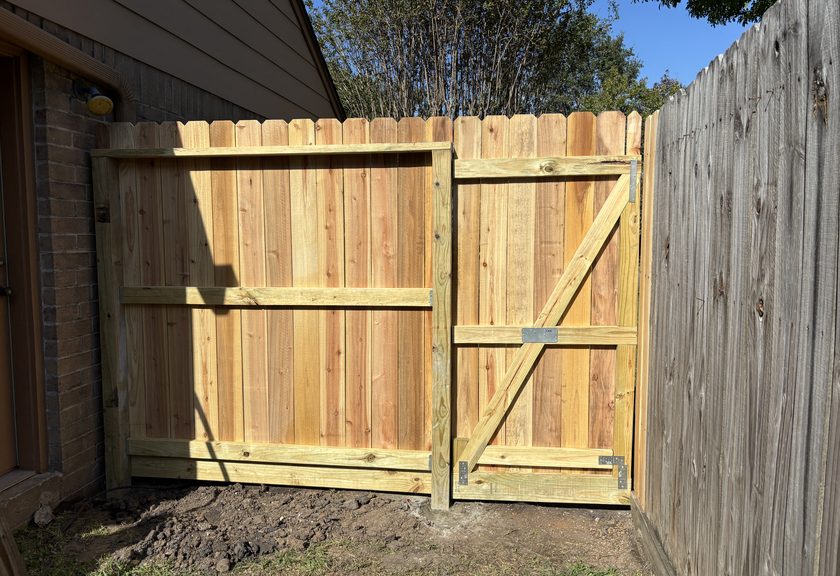 Newly built wood double gate between a brick house and an older gray fence