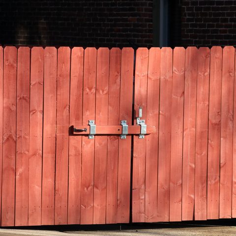 Red-stained wood double gate closed with a slide bolt